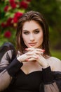 Beautiful girl in the garden with roses. Portrait of a woman with big lips in black clothes on a background of red flowers. Greens Royalty Free Stock Photo