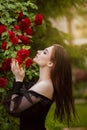 Beautiful girl in the garden with roses. Portrait of a woman with big lips in black clothes on a background of red flowers. Greens Royalty Free Stock Photo