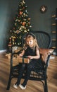 Beautiful girl with gift box in hands sitting in chair Christmas interior
