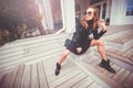 Beautiful girl in glam rock style wear sitting on a steps, drinking street coffee and posing on camera. Feeling of freedom Royalty Free Stock Photo