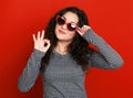 Beautiful girl glamour portrait on red in heart shape sunglasses, long curly hair