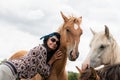 A beautiful girl in glasses and with a bandana on her head strokes the horses in the meadow. Blurred background