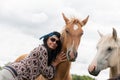 A beautiful girl in glasses and with a bandana on her head strokes the horses in the meadow. Blurred background