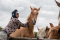 A beautiful girl in glasses and with a bandana on her head strokes the horses in the meadow. Blurred background