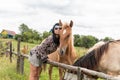 A beautiful girl in glasses and with a bandana on her head strokes the horses in the meadow. Blurred background