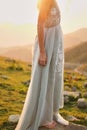 fine-art wedding. Beautiful girl with gorgeous slim in gray dress with hand-painted flowers stands against the mountain landscape