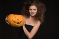 Beautiful girl with a make-up as a witch smiles and holds an orange pumpkin on a black background for the holiday of Halloween Royalty Free Stock Photo