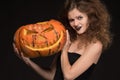 Beautiful girl with a make-up as a witch smiles and holds an orange pumpkin on a black background for the holiday of Halloween Royalty Free Stock Photo