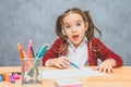 Beautiful girl on gray background. Taking a blue pencil looks into the camera. On the table there are rose-colored Royalty Free Stock Photo