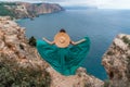 A beautiful girl in a green dress runs to the sea, against the background of large rocks and the sea Royalty Free Stock Photo