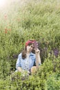 Beautiful girl with a guitar in poppies. Young woman on the grass. A teenager in a denim jacket and a red bandage. Retro Royalty Free Stock Photo