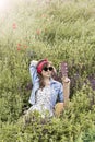 Beautiful girl with a guitar in poppies. Young woman in sunglasses on the grass. A teenager in a denim jacket and a red bandage. Royalty Free Stock Photo