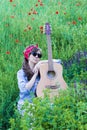 Beautiful girl with a guitar in poppies. Young woman in sunglasses on the grass. A teenager in a denim jacket and a red Royalty Free Stock Photo