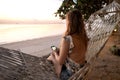 Beautiful girl in a hammock looks at the sunset by the sea