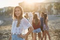 Beautiful girl with hand on hip standing on beach with friends b