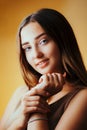 Beautiful girl with hands near face on orange colored background, young woman portrait, concept of female beauty Royalty Free Stock Photo