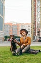 Beautiful girl in a hat and with a dog sitting on a green lawn, the girl holds a puppy on a leash and looks into the camera. Royalty Free Stock Photo