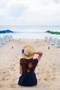 Beautiful girl in a hat sits with her back on a sandy beach and looks on sea Royalty Free Stock Photo