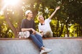 Beautiful girl with headphones and young guy with skateboard happily spending time together at skatepark Royalty Free Stock Photo