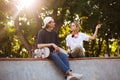 Beautiful girl with headphones and young guy with skateboard thoughtfully discussing something together while spending Royalty Free Stock Photo