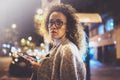 Beautiful girl hipster wearing glasses holding smart phone hands, during night walking in european vocation. Bokeh and Royalty Free Stock Photo