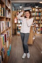 Beautiful girl is holding stack of books while standing among books in the bookshop Royalty Free Stock Photo