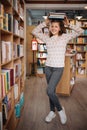Beautiful girl is holding stack of books while standing among books in the bookshop Royalty Free Stock Photo