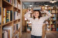 Beautiful girl is holding stack of books while standing among books in the bookshop Royalty Free Stock Photo