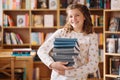 Beautiful girl is holding stack of books while standing among books in the bookshop Royalty Free Stock Photo