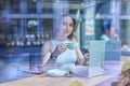 Beautiful girl inside cafe with cup of coffee by laptop looking through window