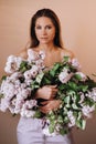 Beautiful girl with lilac flowers in her hands. A girl with lilac flowers in the spring at home. A girl with long hair and lilac