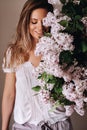 Beautiful girl with lilac flowers in her hands. A girl with lilac flowers in the spring at home. A girl with long hair and lilac