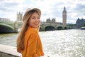 Beautiful girl in London, UK. Portrait of young stylish woman in orange shirt and hat looking at camera with Westminster Bridge on Royalty Free Stock Photo