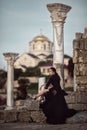 A beautiful girl in a long black dress with her legs open, poses at sunset amid antique columns, churches and ruins. Royalty Free Stock Photo