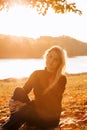 Beautiful girl with long blond hair in autumn landscape at sunset. Girl sitting on the grass, selective focus Royalty Free Stock Photo