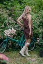 Beautiful girl with long blonde hair holds pink peony flowers while standing near a retro bike Royalty Free Stock Photo