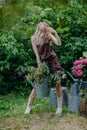 Beautiful girl with long blonde hair holds a watering can with flowers in a blooming garden Royalty Free Stock Photo