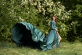 A beautiful girl in a long green silk dress on the background of a flowering tree. The hem of the dress develops in the wind . Cop Royalty Free Stock Photo