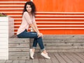 Beautiful girl with long hair brunette in jeans sits near wall of orange old white wooden planks