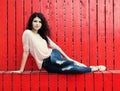 Beautiful girl with long hair brunette in jeans sits near wall of red wooden planks