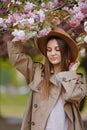 Beautiful girl with long hair holding sakura branch among pink cherry blossoms in spring. Model wearing stylish accessories and cl Royalty Free Stock Photo