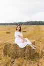 Girl with long hair in a long white dress sitting on a haystack in a field Royalty Free Stock Photo