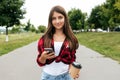 Beautiful girl with long hair teenager 11-12 years old, standing in summer in city park. In hands of a smartphone and a Royalty Free Stock Photo