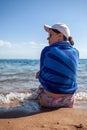 A beautiful girl with long hair and a white cap looks at the blue sea Royalty Free Stock Photo