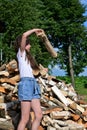 beautiful girl with long hair in white T-shirt and denim shorts puts firewood in pile. Royalty Free Stock Photo