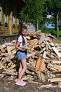 beautiful girl with long hair in white T-shirt and denim shorts puts firewood in pile. Royalty Free Stock Photo