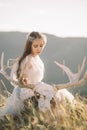 Beautiful girl in a long white grey curly dress is made of tulle in the nature, in the mountains sits the forest, a hand removes