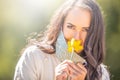 Beautiful girl looks at the camera smelling a flower, wearing only one half of her polka dot face mask Royalty Free Stock Photo