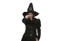 Beautiful girl in looks like sorceress isolated on white background. Woman wears black pointed hat, coat with magic wand