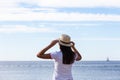 Beautiful girl looks at the sea. Young girl in a hat looking at a calm sea and blue skies Royalty Free Stock Photo